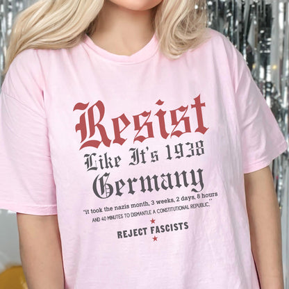 May include: Pink t-shirt with a black and red graphic that says "Resist Like It's 1938 Germany" and "Reject Fascists". The graphic also includes the text "it took the nazis month, 3 weeks, 2 days, 8 hours and 40 minutes to dismantle a constitutional republic."