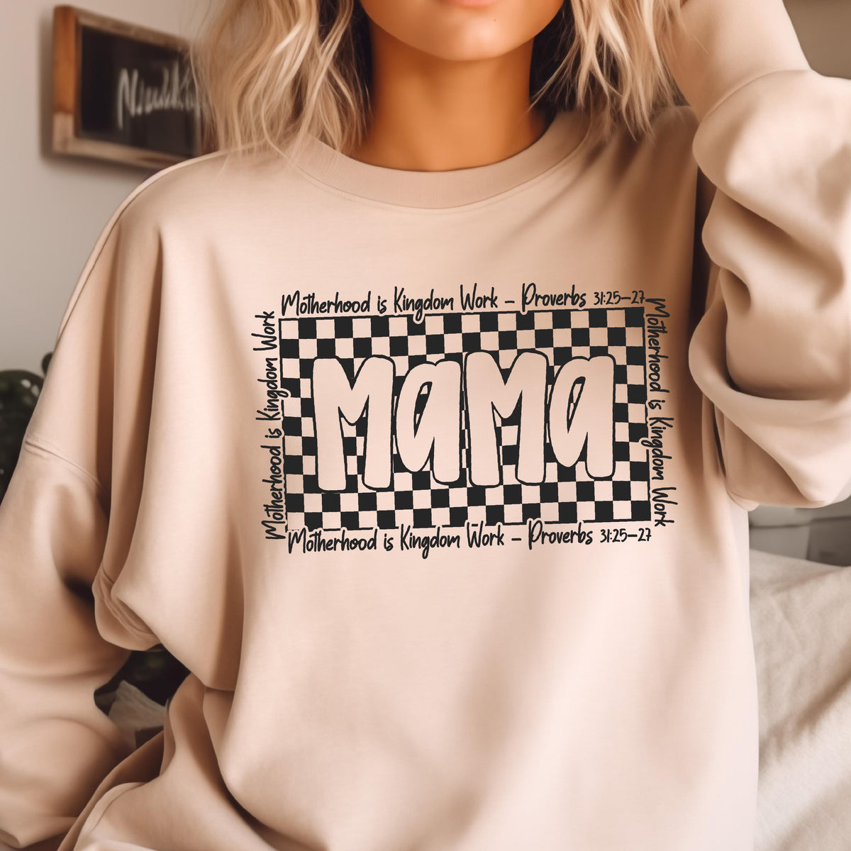 May include: A beige sweatshirt with a black checkered design and the word "Mama" in a white outline. The text "Motherhood is Kingdom Work - Proverbs 3:25-27" is written around the checkered design.