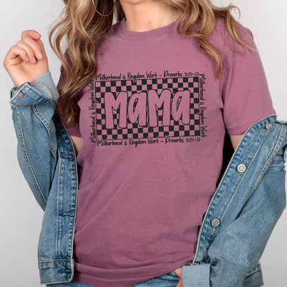 May include: A mauve t-shirt with a black and white checkered design and the word "Mama" in pink letters. The text "Motherhood is Kingdom Work - Proverbs 3:25-27" is printed on the shirt.