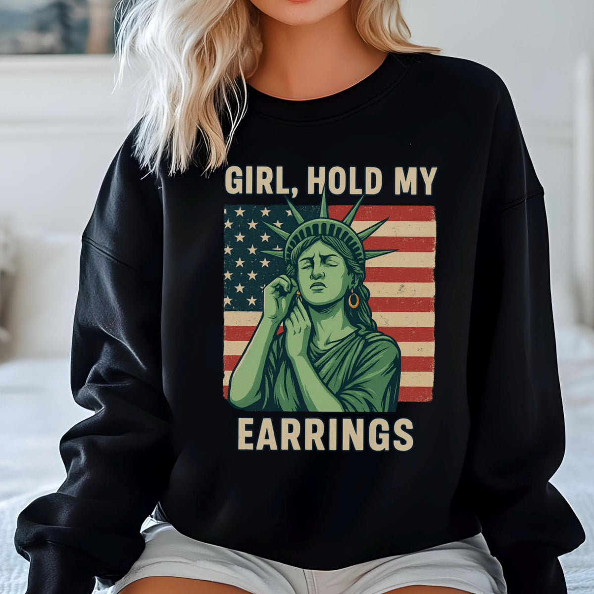 May include: Black sweatshirt with a graphic of the Statue of Liberty holding her ear and the text "Girl, Hold My Earrings" printed on it. The graphic is set against a red, white, and blue American flag.