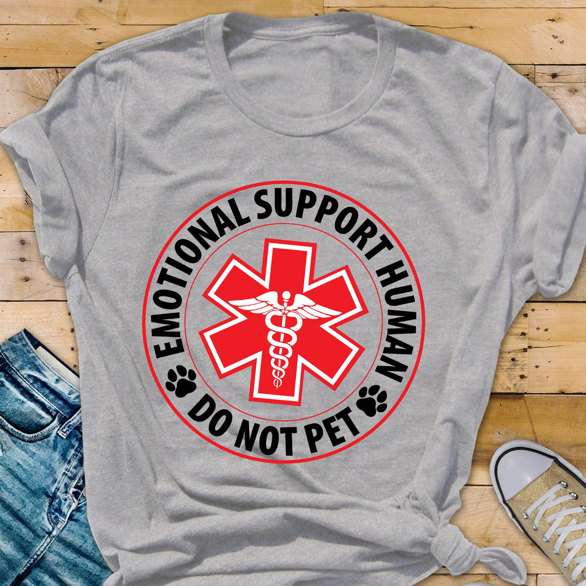 May include: A gray t-shirt featuring a red medical symbol with the words "EMOTIONAL SUPPORT HUMAN" and "DO NOT PET" in a circular design. The shirt has a crew neck and short sleeves.