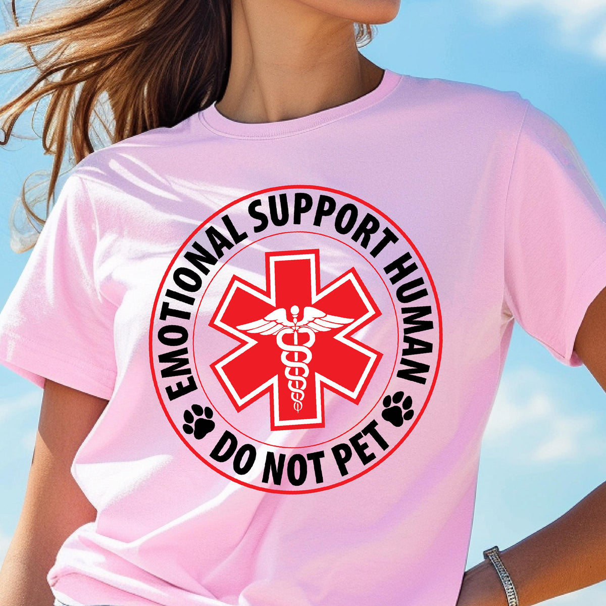 May include: A light pink t-shirt with a circular graphic that reads "EMOTIONAL SUPPORT HUMAN" and "DO NOT PET". The graphic features a red star with a medical symbol and paw prints. The shirt is short-sleeved.