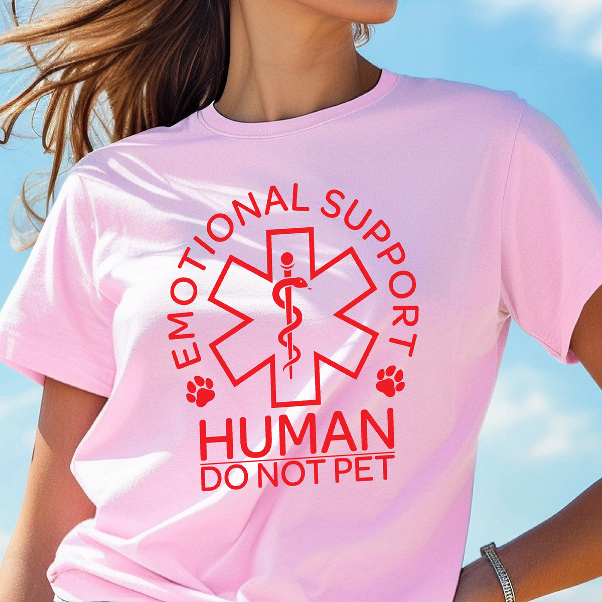 May include: A light pink t-shirt featuring a red graphic of a six-pointed star with a rod and snake symbol in the center. The text reads EMOTIONAL SUPPORT HUMAN DO NOT PET, accompanied by two small paw print icons on either side of the star design.