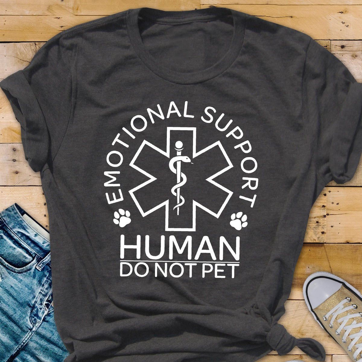 May include: A dark gray short-sleeved t-shirt featuring a white graphic of a Star of Life symbol with a snake and staff. The text reads EMOTIONAL SUPPORT HUMAN DO NOT PET, accompanied by two small paw print icons on either side of the central emblem.