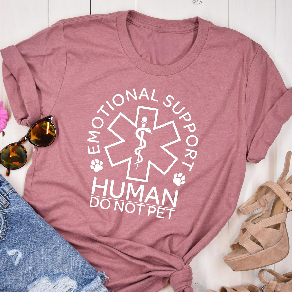 May include: A mauve short-sleeved t-shirt featuring a white graphic of a six-pointed star with a central staff and snake symbol. The text reads EMOTIONAL SUPPORT HUMAN DO NOT PET, accompanied by two small paw print icons on either side of the star.