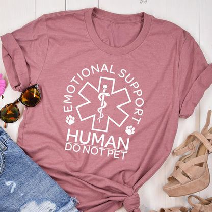 May include: A mauve short-sleeved t-shirt featuring a white graphic of a six-pointed star with a central staff and snake symbol. The text reads EMOTIONAL SUPPORT HUMAN DO NOT PET, accompanied by two small paw print icons on either side of the star.