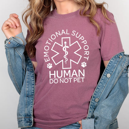 May include: A mauve short-sleeved t-shirt featuring a white graphic of a six-pointed star with a serpent-entwined staff in the center. The text reads EMOTIONAL SUPPORT HUMAN DO NOT PET, accompanied by two small paw print icons on either side.