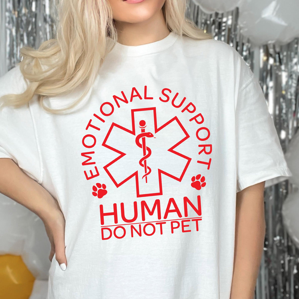 May include: A white short-sleeved t-shirt featuring a red graphic of a Star of Life symbol with a snake and staff. The text reads EMOTIONAL SUPPORT HUMAN DO NOT PET, accompanied by two small red paw prints on either side of the central emblem.