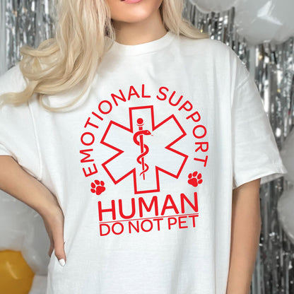 May include: A white short-sleeved t-shirt featuring a red graphic of a Star of Life symbol with a snake and staff. The text reads EMOTIONAL SUPPORT HUMAN DO NOT PET, accompanied by two small red paw prints on either side of the central emblem.