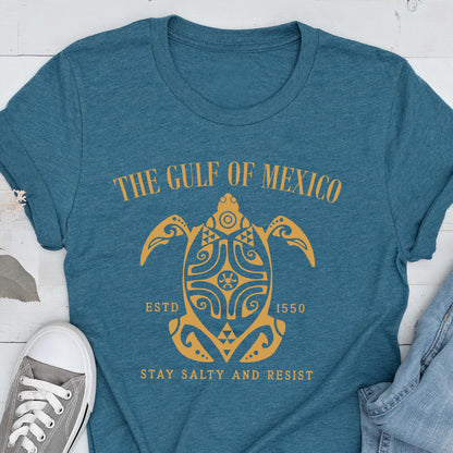 May include: A teal blue t-shirt with a gold graphic of a stylized turtle with the text "The Gulf of Mexico" above it and "Estd 1550" and "Stay Salty and Resist" below it.