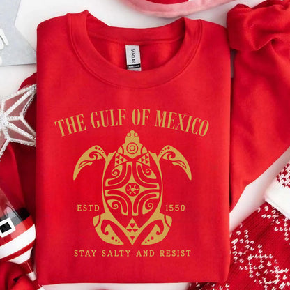 May include: Red sweatshirt with a gold graphic of a turtle with the text "The Gulf of Mexico" above it and "Estd 1550" and "Stay Salty and Resist" below it.