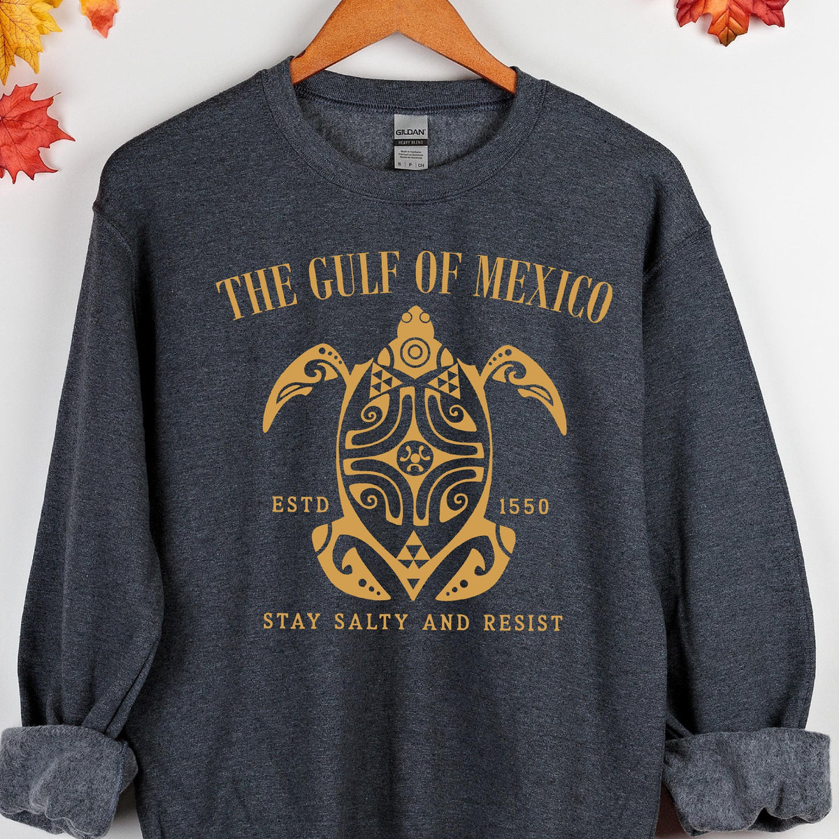 May include: A dark gray sweatshirt with a gold graphic of a sea turtle with the text "The Gulf of Mexico" above it, "Est. 1550" below it, and "Stay Salty and Resist" at the bottom.