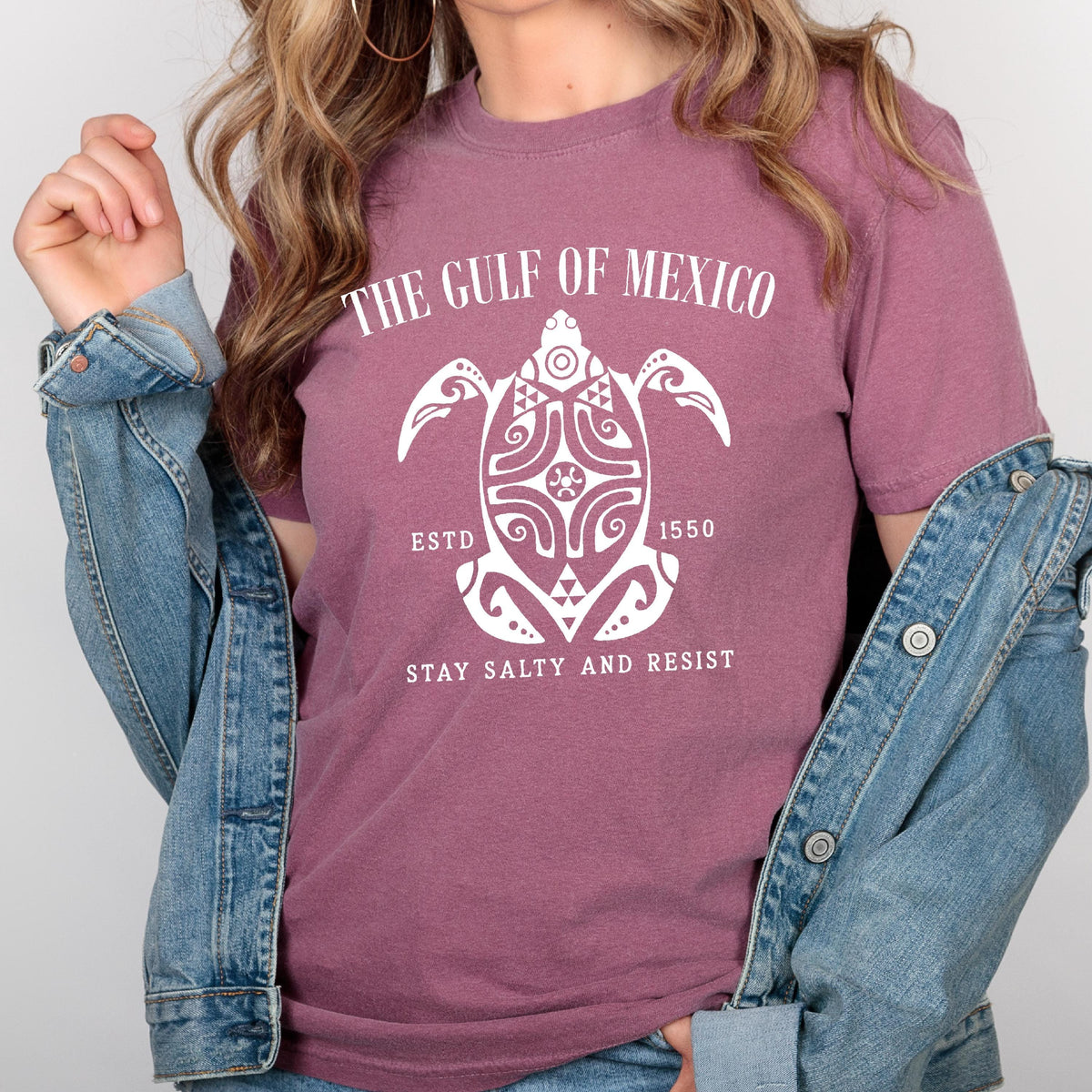 May include: A mauve t-shirt with a white graphic of a stylized turtle with the text "The Gulf of Mexico, Est'd 1550, Stay Salty and Resist".