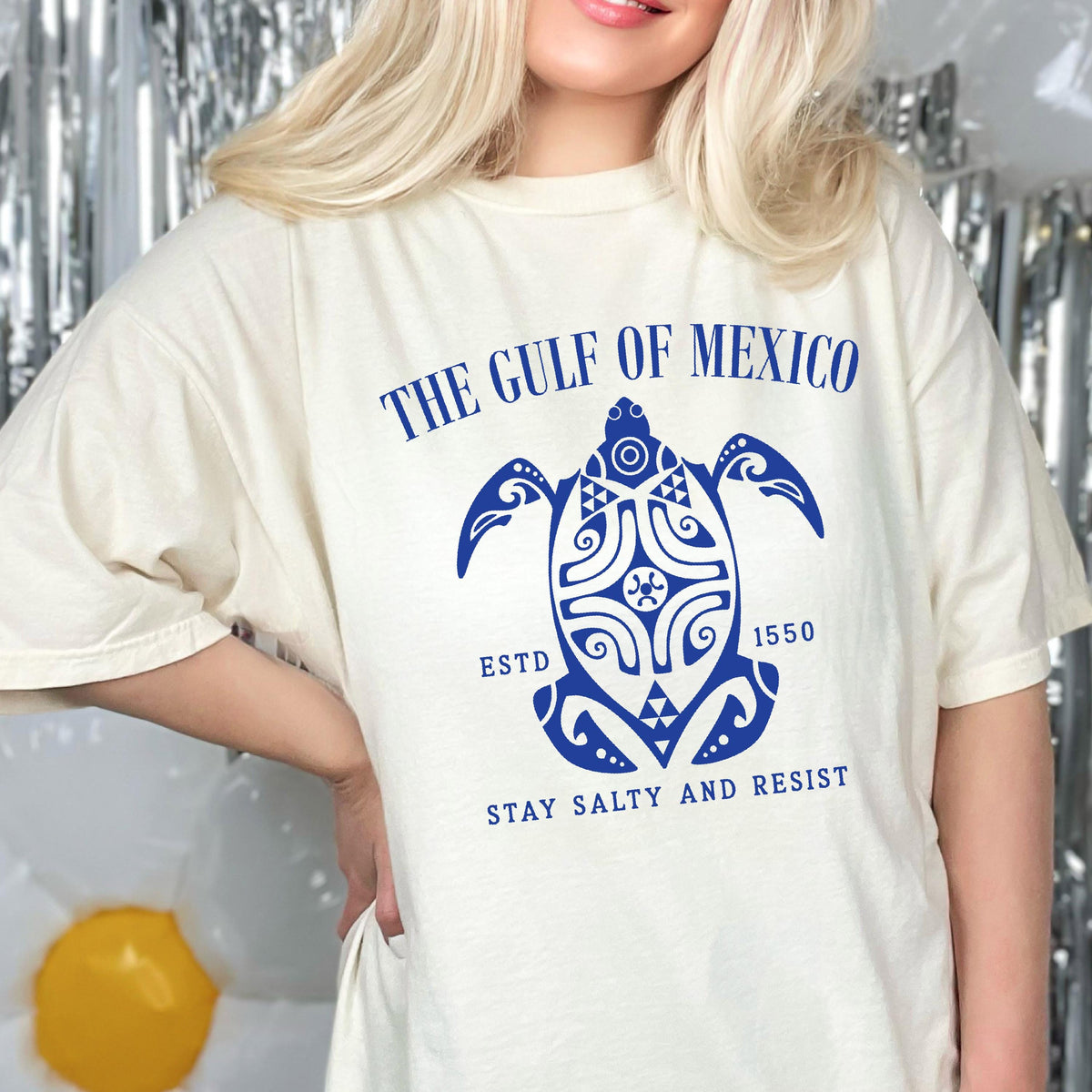 May include: A white t-shirt with a blue graphic of a stylized turtle with the text "The Gulf of Mexico Est. 1550 Stay Salty and Resist".