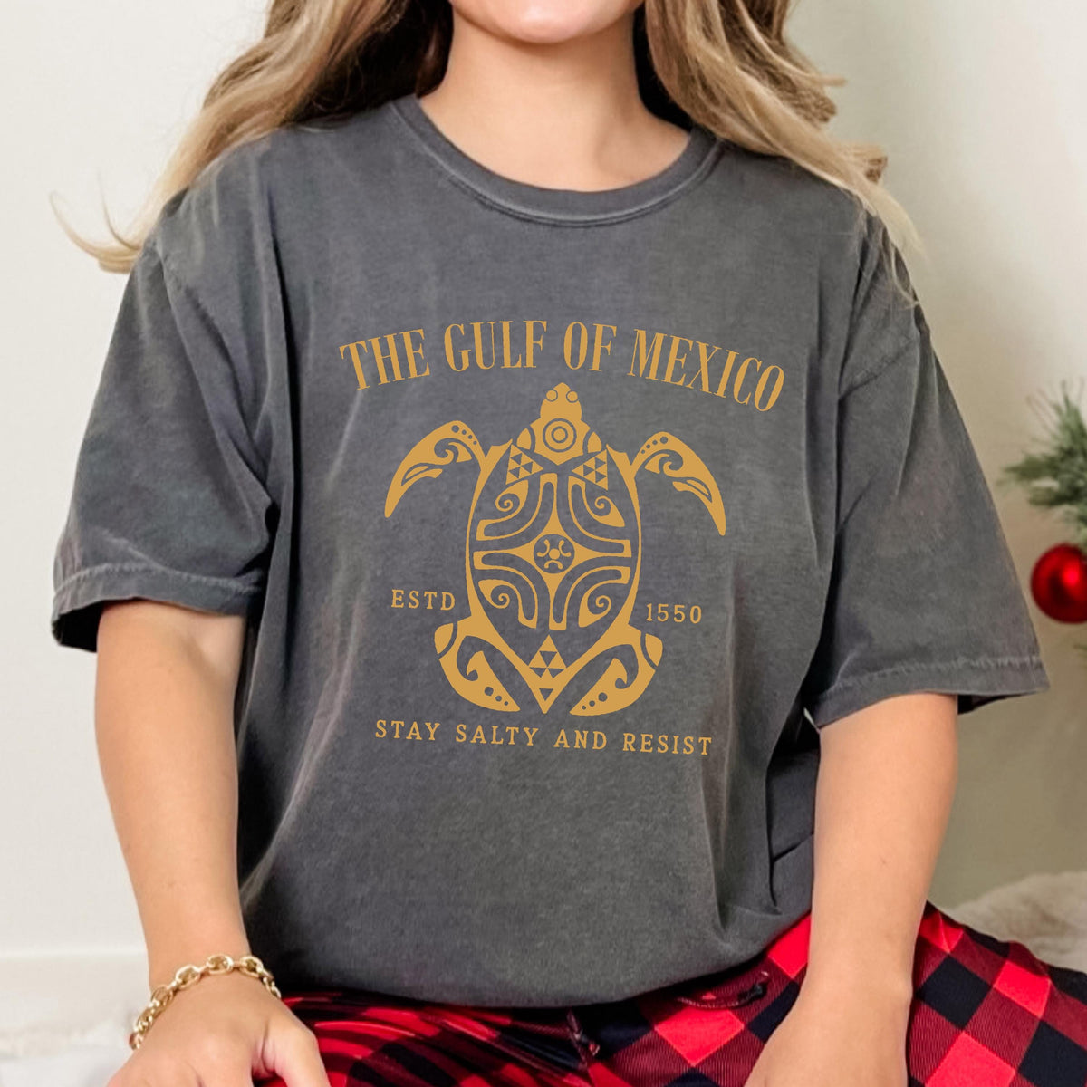May include: A gray t-shirt with a vintage look featuring a gold graphic of a stylized turtle with the text "The Gulf of Mexico" above it, "Est'd 1550" below it, and "Stay Salty and Resist" at the bottom.