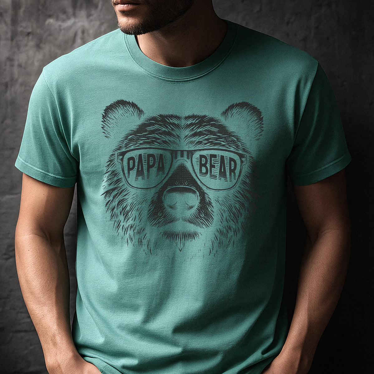 May include: Teal green t-shirt featuring a graphic of a bear's face wearing sunglasses. The sunglasses have the words "PAPA BEAR" printed on them. The bear graphic is in black and white.
