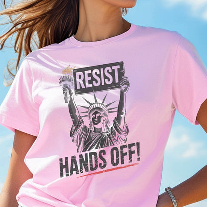 May include: Pink t-shirt with a graphic of the Statue of Liberty holding a sign that says "Resist" and the text "Hands Off!"