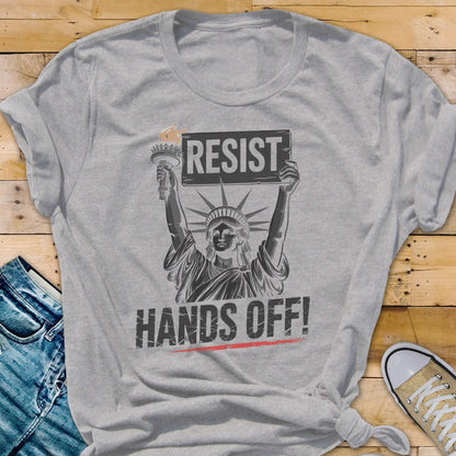 May include: Gray t-shirt with a graphic of the Statue of Liberty holding a sign that says "Resist" and the text "Hands Off!" below.