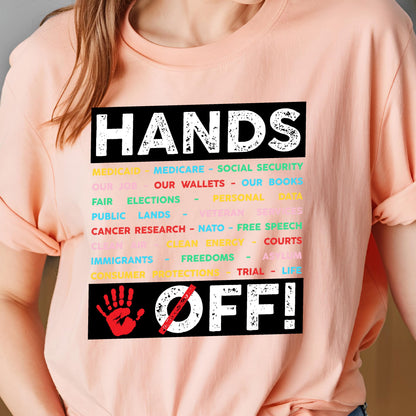 May include: Pink t-shirt with the text "HANDS OFF!" in black. The text is surrounded by a list of items in various colors, including "Medicare", "Social Security", "Our Wallets", "Our Books", "Fair Elections", "Public Lands", "Veteran Services", "Cancer Research", "NATO", "Free Speech", "Clean Air", "Clean Energy", "Courts", "Immigrants", "Freedoms", "Asylum", "Consumer Protections", "Trial", and "Life". A red handprint with a diagonal line through it is below the text.