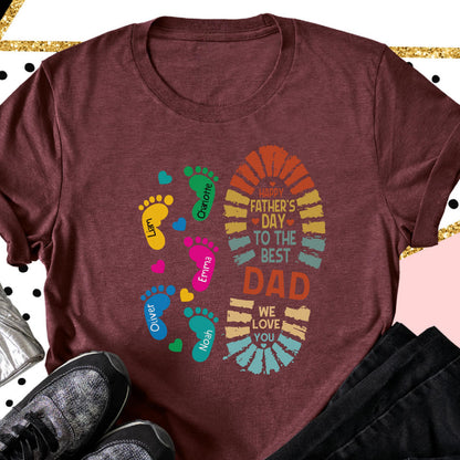 May include: Maroon t-shirt with a colorful graphic for Father's Day. The design includes a large footprint with the text "Happy Father's Day To The Best Dad We Love You." Smaller footprints with names are also included.