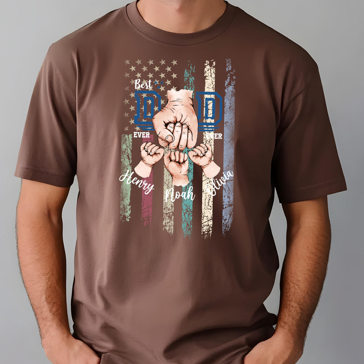 May include: Brown t-shirt featuring a graphic of an American flag with the words "Best Dad Ever" and the names "Henry, Noah, Olivia". The design includes illustrations of hands and fists.