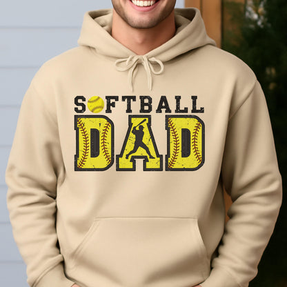 May include: A tan hoodie with the words "SOFTBALL DAD" in yellow and black. The word "DAD" features a silhouette of a batter. A yellow softball is above the word "SOFTBALL".