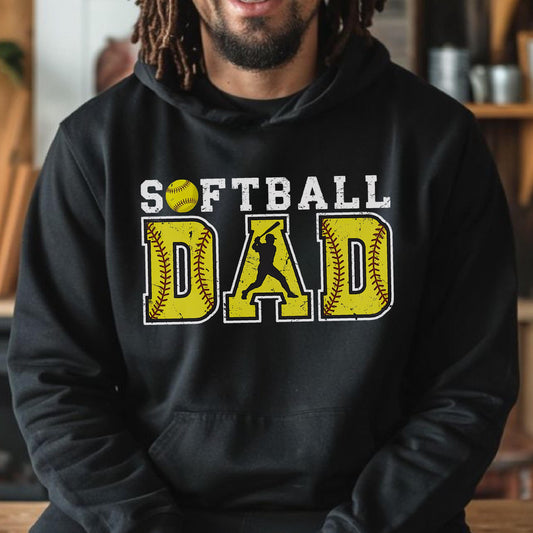 May include: Black hooded sweatshirt with the words "SOFTBALL DAD" in white and yellow. The word "DAD" is designed to look like a softball with a batter silhouette in the center. The softball and the word "DAD" are yellow with a distressed texture.