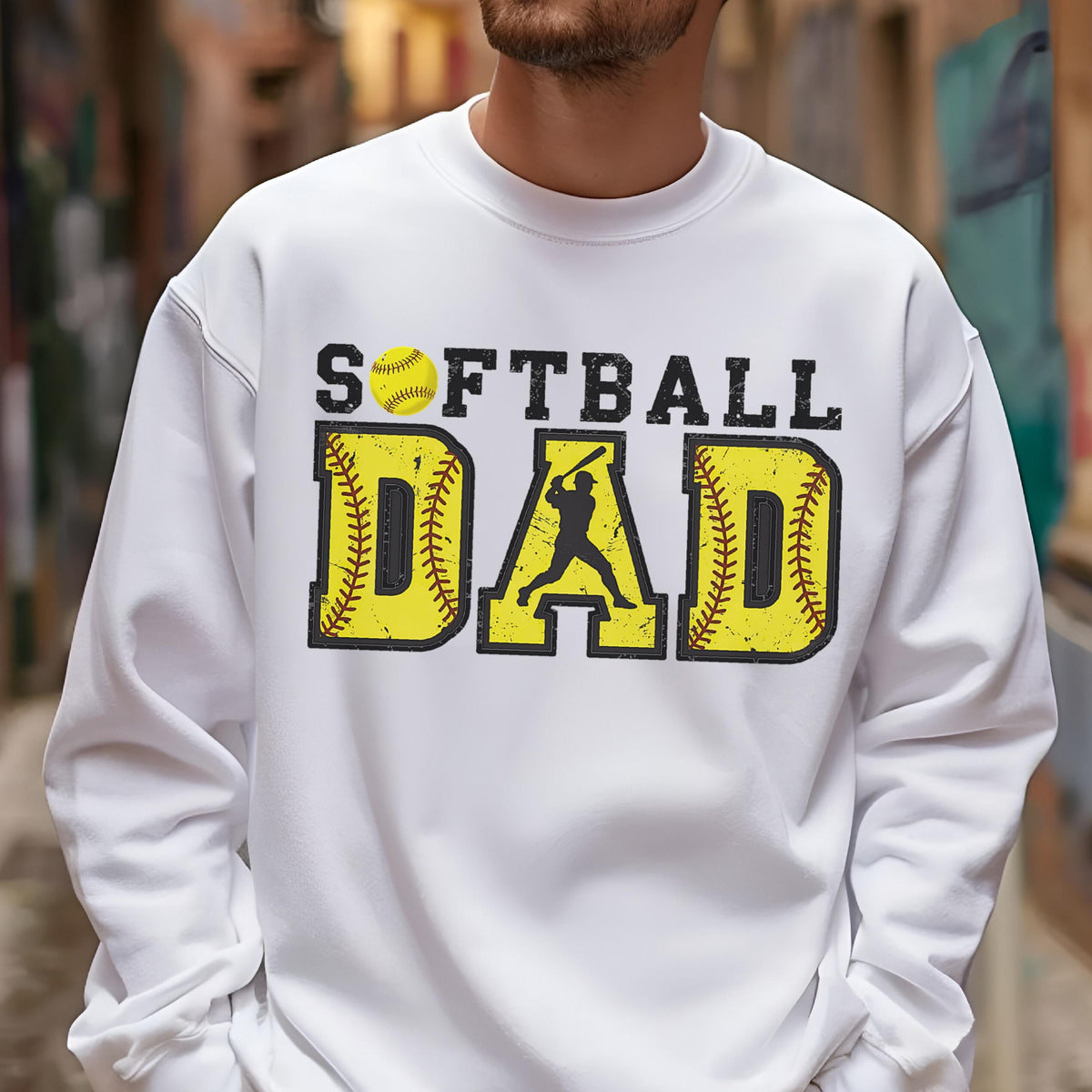 May include: White sweatshirt with the words "SOFTBALL DAD" in black and yellow. The word "DAD" is in a baseball-style font with a batter silhouette. A yellow softball is above the word "SOFTBALL".