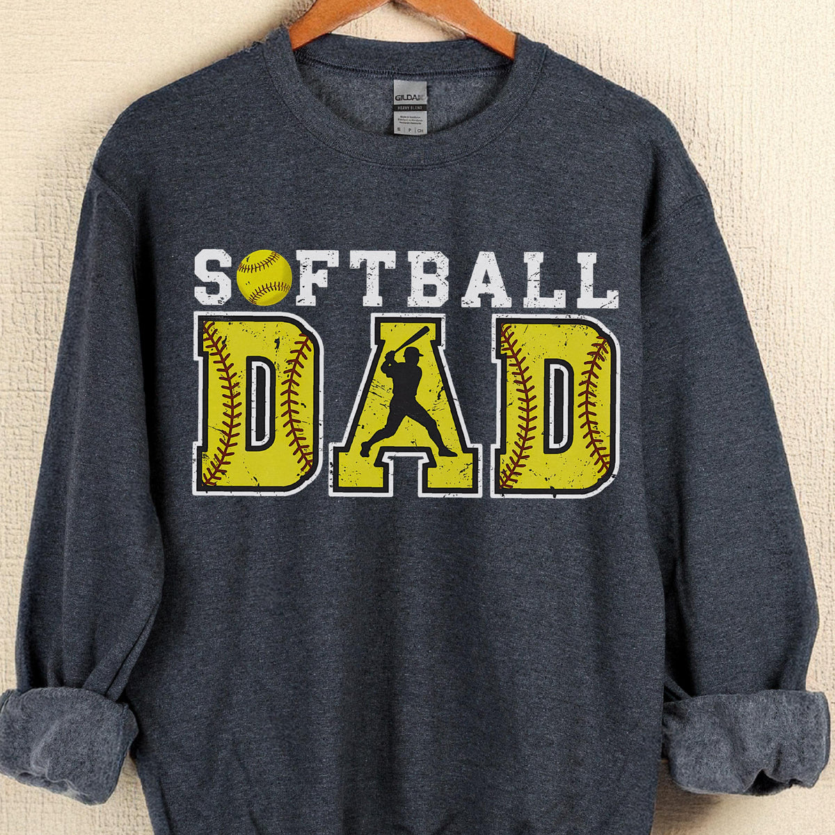 May include: A dark gray sweatshirt with the words "SOFTBALL DAD" in white and yellow. The word "DAD" is designed to look like a softball. A silhouette of a batter is in the center.