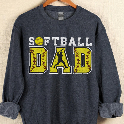 May include: A dark gray sweatshirt with the words "SOFTBALL DAD" in white and yellow. The word "DAD" is designed to look like a softball. A silhouette of a batter is in the center.