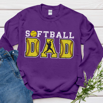 May include: A purple sweatshirt with the words "SOFTBALL DAD" in white and yellow. The word "SOFTBALL" has a yellow softball graphic. The word "DAD" has a yellow baseball graphic with a batter silhouette.