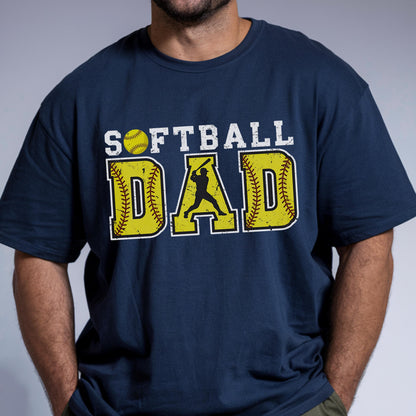 May include: A navy blue t-shirt with the text "Softball Dad" in white with yellow baseballs and a silhouette of a softball player.