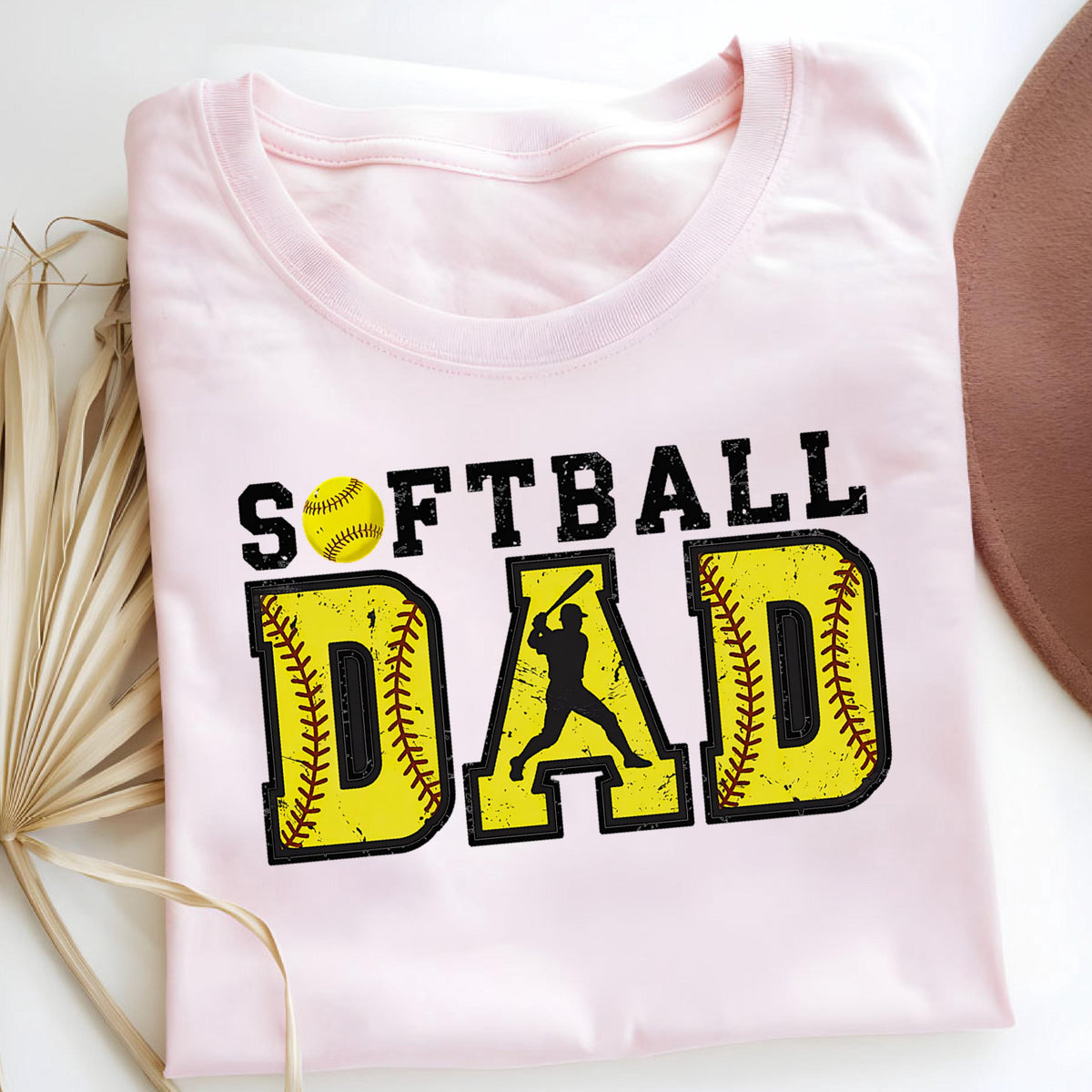 May include: Pink t-shirt with the text "Softball Dad" in black and yellow. The text is surrounded by a yellow softball with red stitching.