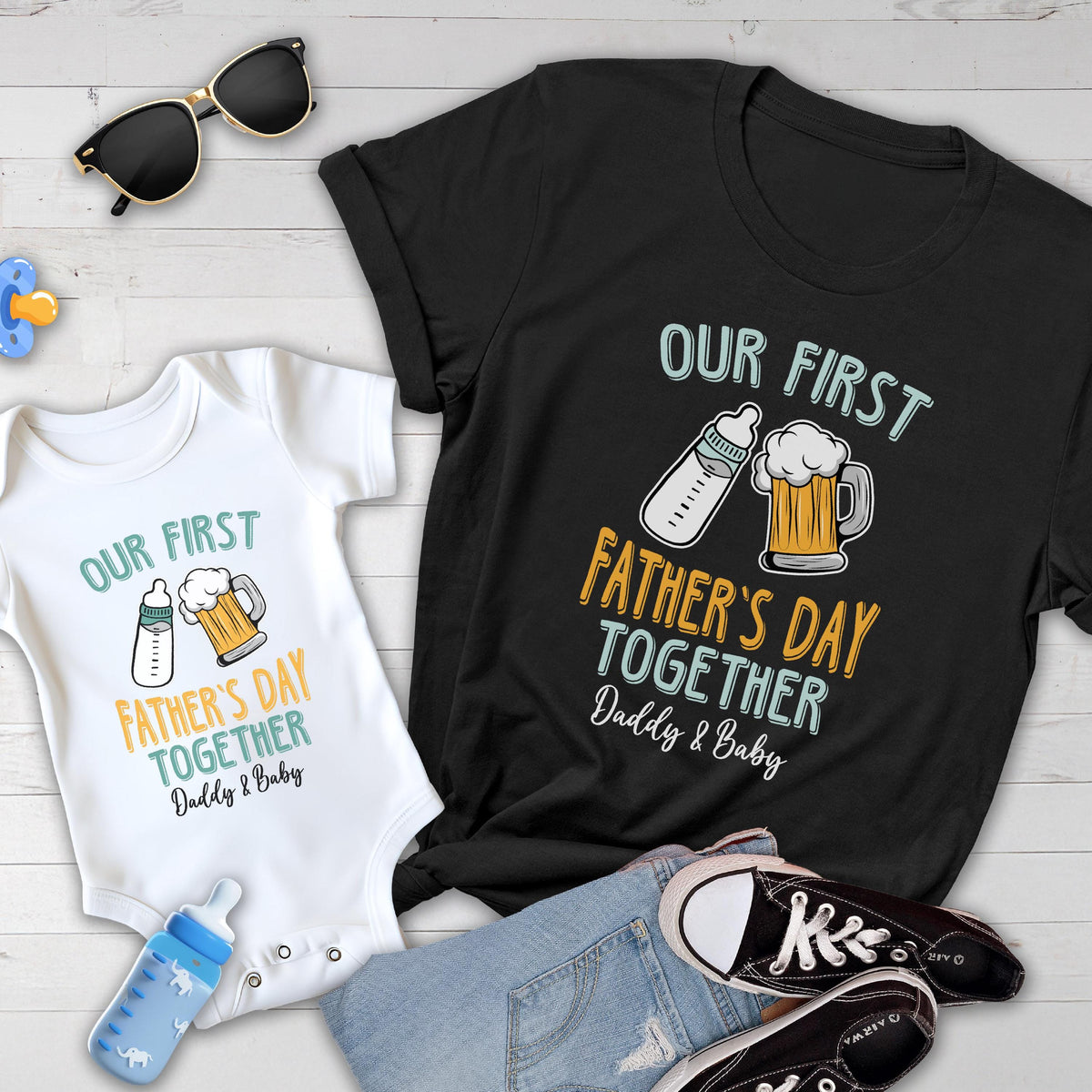 May include: A white onesie and a black t-shirt with the text "Our First Father's Day Together Daddy & Baby" and illustrations of a baby bottle and a beer mug.