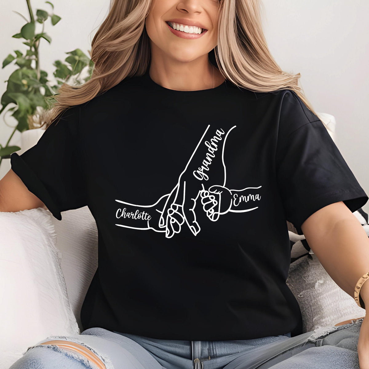 May include: Black t-shirt with a white graphic of three hands holding each other. The word "Grandma" is written in cursive on one hand, and the names "Charlotte" and "Emma" are written on the other hands.