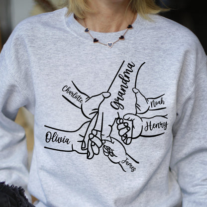 May include: A light gray sweatshirt featuring a black line drawing of hands clasped together. The word "Grandma" is written in cursive, with the names "Charlotte", "Olivia", "Noah", "Henry", and "James" also written in cursive.