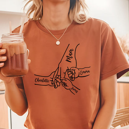 May include: A rust-colored short-sleeve t-shirt featuring a black line art graphic of multiple hands holding fingers together. The text Mam, Charlotte, Emma, and James is printed in a cursive script alongside the corresponding hand illustrations.