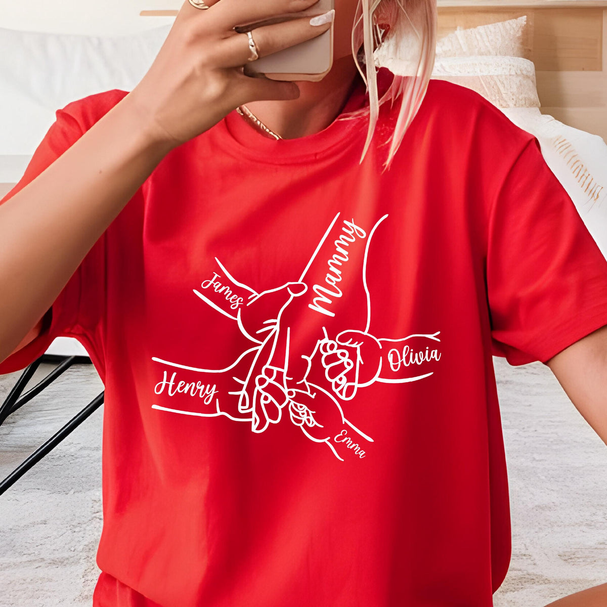 May include: A bright red short-sleeved t-shirt featuring a white line-art graphic of multiple hands holding each other. The design includes the names James, Mammy, Henry, Olivia, and Emma written in a cursive script integrated into the hand illustration.