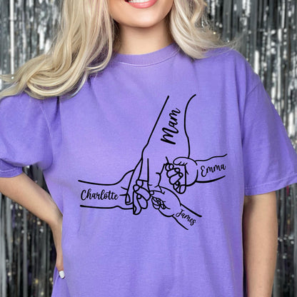 May include: A light purple short-sleeve t-shirt featuring a black line art graphic of multiple hands holding each other. The design includes the printed names Mam, Charlotte, Emma, and James positioned near the corresponding hand illustrations.