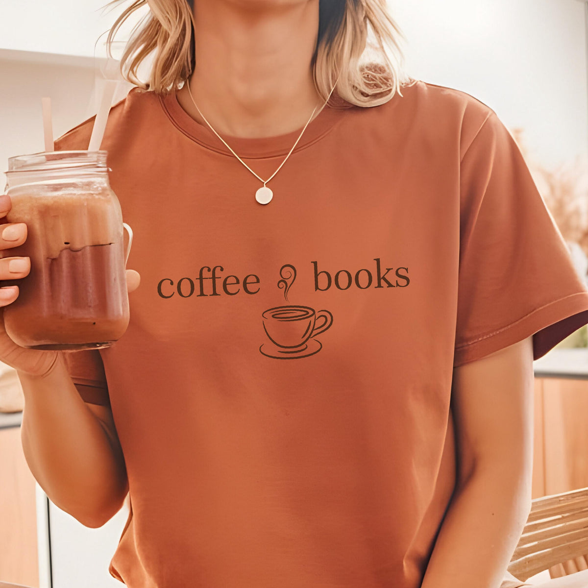 May include: A rust-colored short-sleeve t-shirt featuring the black text "coffee & books" centered on the chest, accompanied by a small graphic of a steaming coffee cup. The shirt has a crew neckline and a simple, clean design.