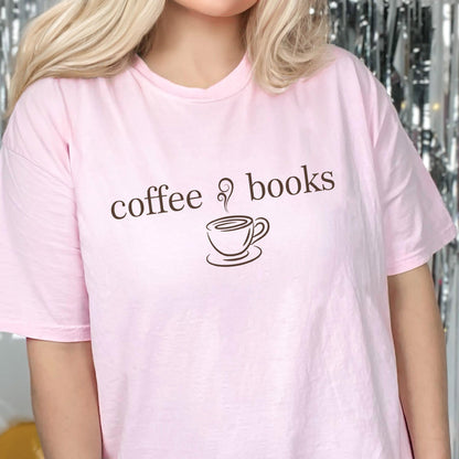 May include: A light pink short-sleeved t-shirt featuring the dark brown text "coffee & books" printed across the chest. Below the text is a simple dark brown line drawing of a steaming coffee cup on a saucer, centered on the front of the garment.