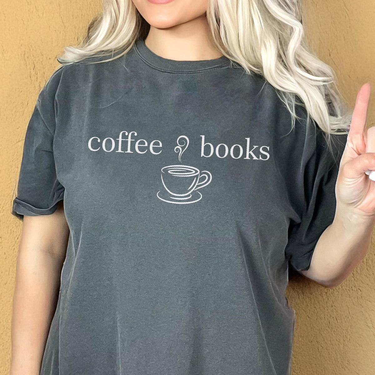 May include: A charcoal gray short-sleeve t-shirt featuring the white text coffee books with a small graphic of a steaming coffee cup centered between the words. The shirt has a crew neckline and a relaxed fit with a slightly faded, washed-out appearance.