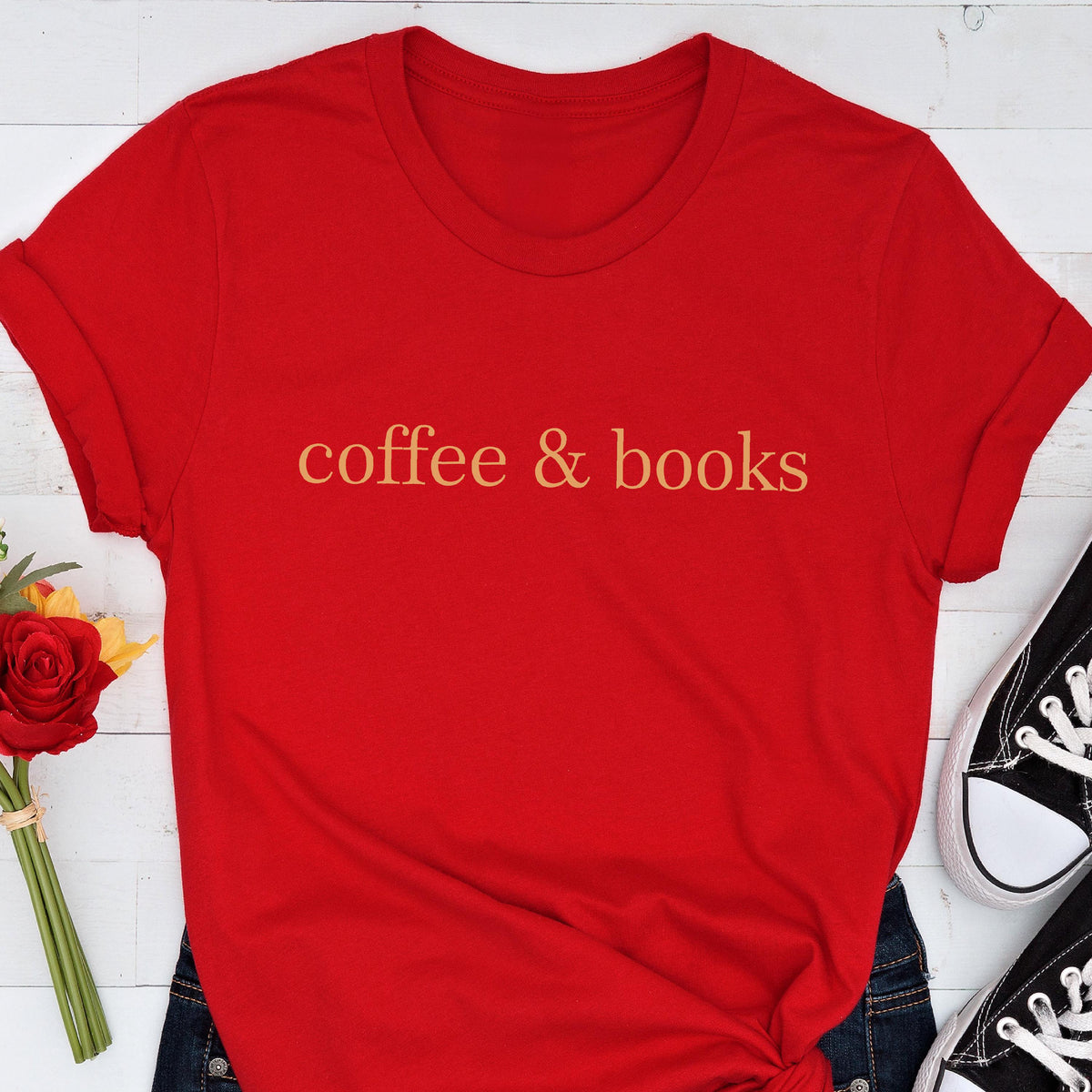 May include: A bright red short-sleeved t-shirt featuring the text coffee & books printed in a gold-toned font across the center of the chest. The garment has a classic crew neckline and rolled sleeves, presenting a simple and clean design.