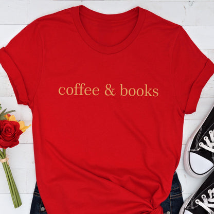 May include: A bright red short-sleeved t-shirt featuring the text coffee & books printed in a gold-toned font across the center of the chest. The garment has a classic crew neckline and rolled sleeves, presenting a simple and clean design.