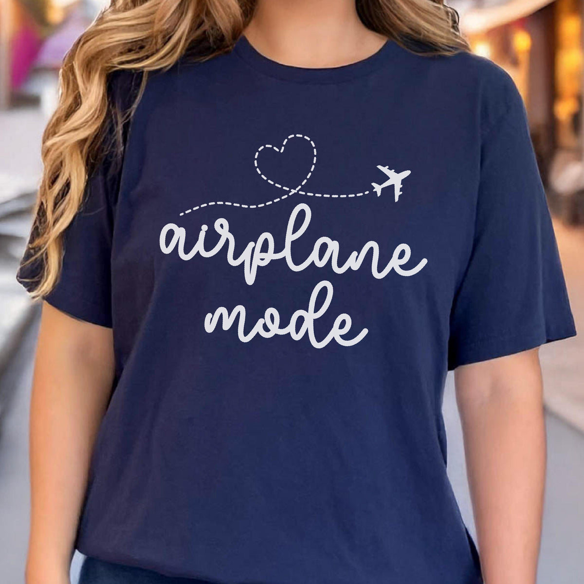 May include: Navy blue t-shirt with the words "airplane mode" in white script, accompanied by a dotted line, a heart, and a small airplane graphic. The shirt is a casual, everyday wear item.