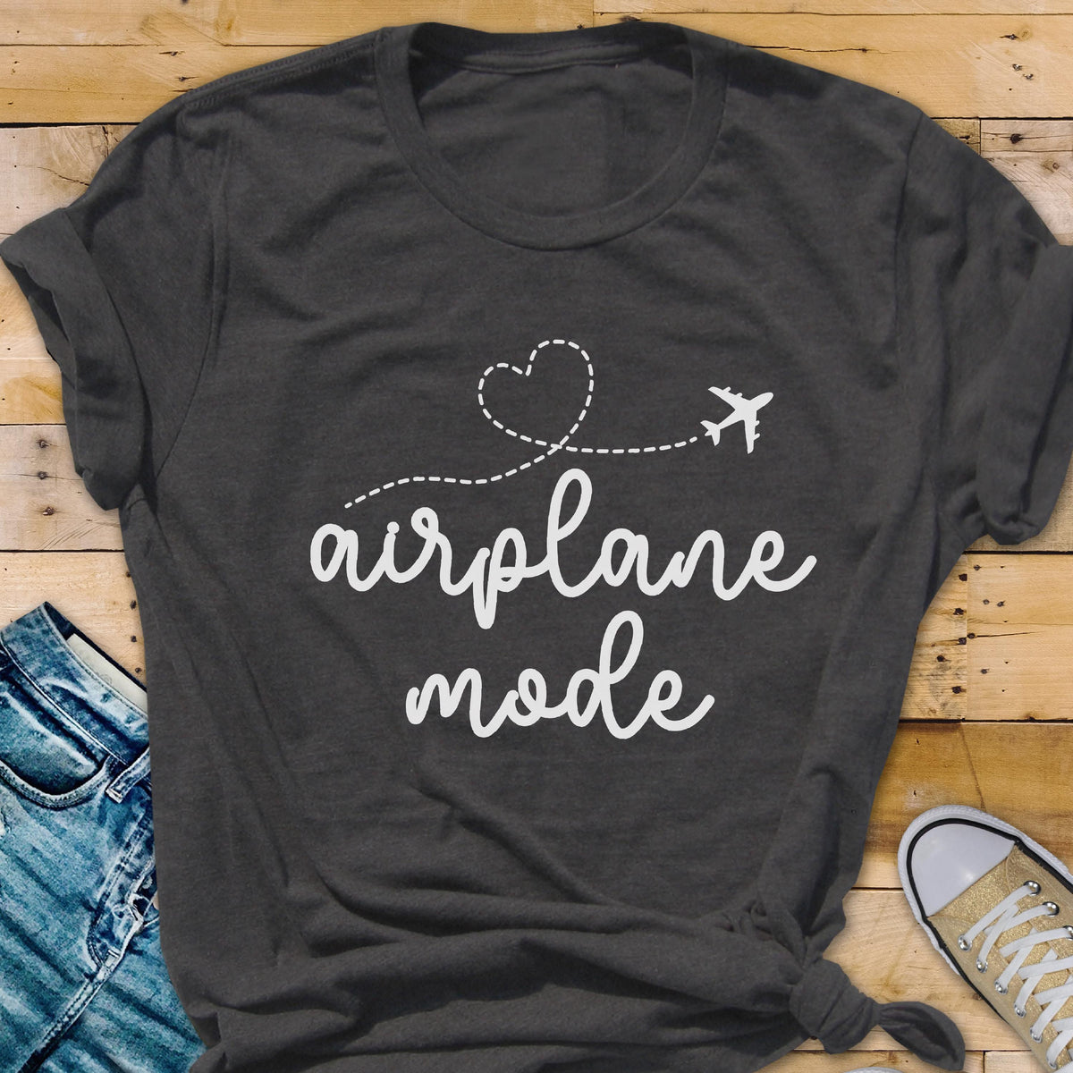 May include: Dark gray t-shirt with the words "airplane mode" in a cursive font. A dotted line with a heart and airplane graphic is above the text. The shirt is folded at the sleeves.