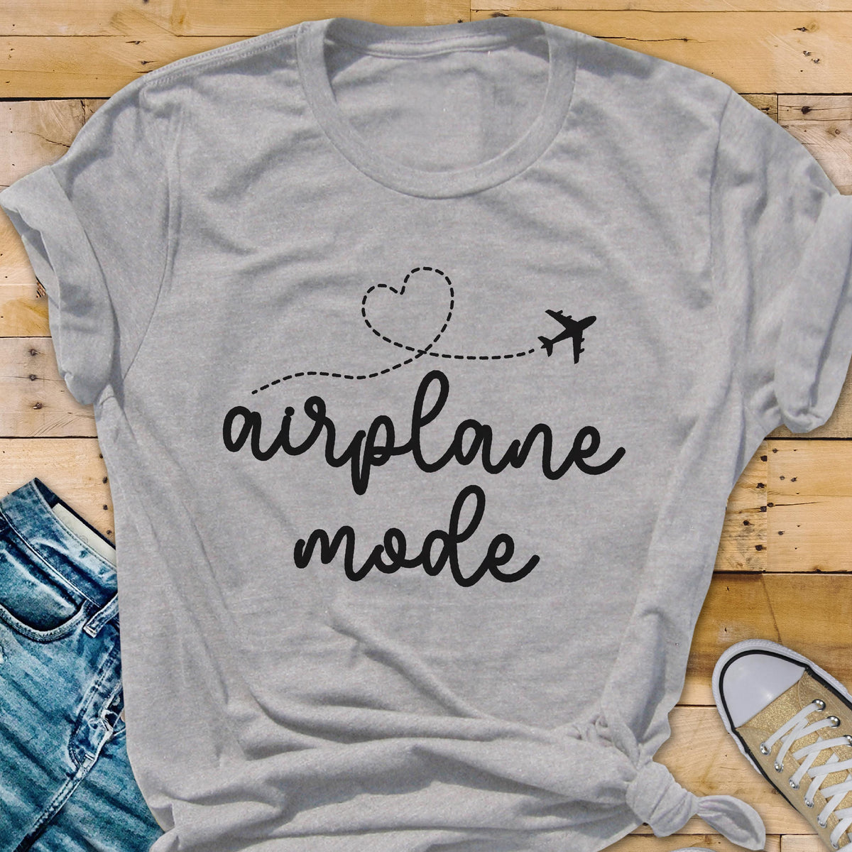 May include: A light gray t-shirt with the words "airplane mode" in a handwritten font. A dotted line forms a heart shape and leads to a small airplane graphic. The shirt is folded at the bottom.