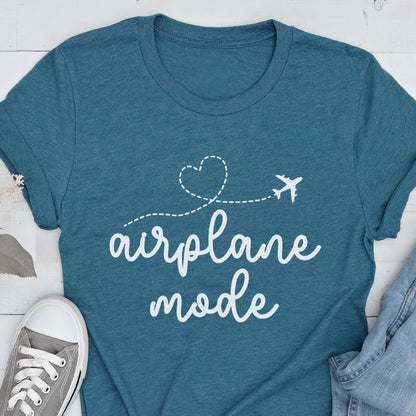May include: Teal t-shirt with the words "airplane mode" in a white script font. A white airplane graphic follows a dotted line that forms a heart shape. A gray sneaker and denim jeans are visible in the image.