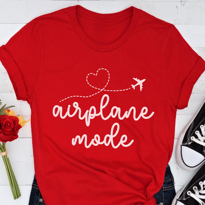 May include: A red t-shirt with the words "airplane mode" in white script. A dotted line with a heart and airplane graphic is above the text. The shirt is folded at the sleeves and is paired with blue jeans and black sneakers.