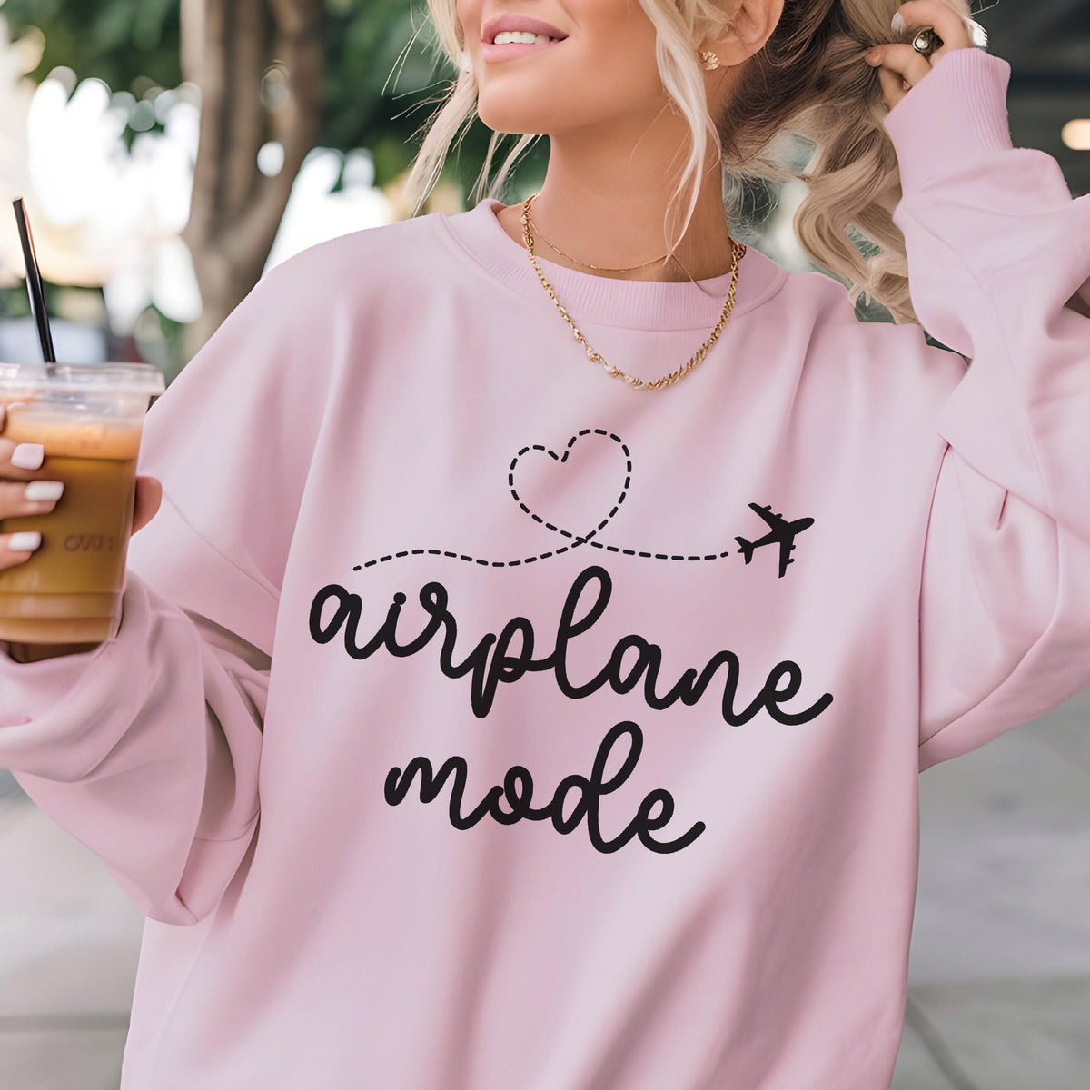 May include: A light pink long-sleeve sweatshirt featuring black text that reads airplane mode. Above the text is a black dashed line forming a heart shape that leads to a small black airplane silhouette. The sweatshirt has a crew neckline.